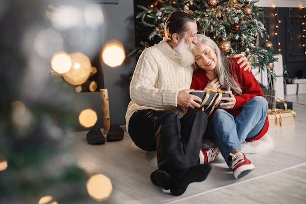 Homem sênior apresentando presente de natal para sua esposa sentada perto da árvore de natal