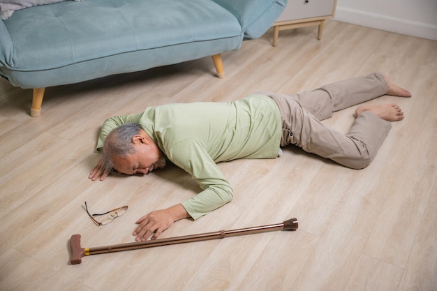 Homem sênior asiático caindo deitado no chão em casa sozinho com bengala de madeira