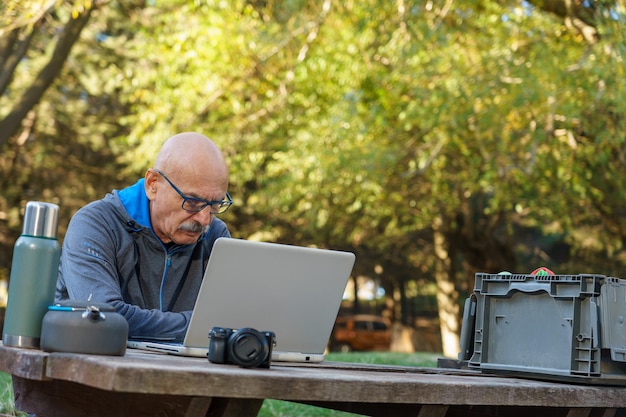 Homem sênior atencioso usando computador na natureza