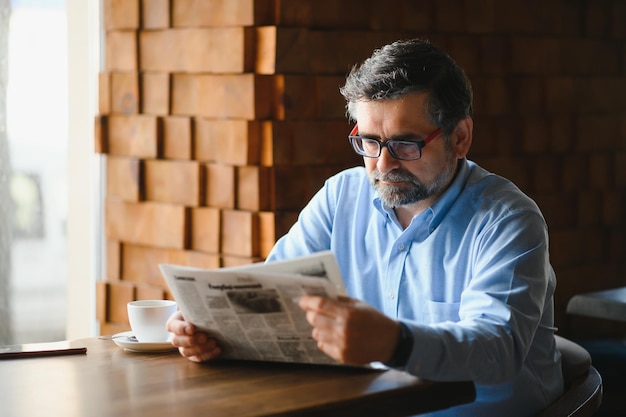 Foto homem sênior ativo lendo jornal e tomando café no restaurante