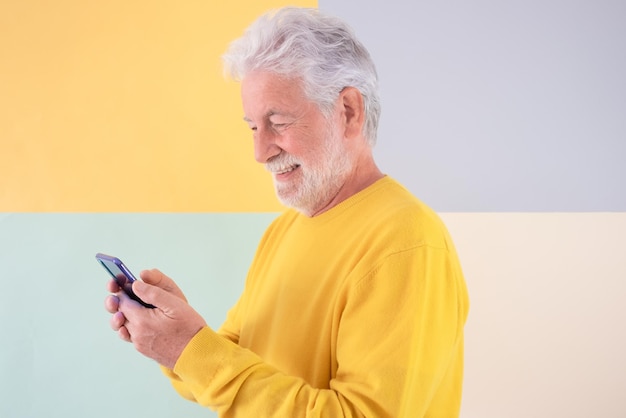 Homem sênior barbudo sorridente em amarelo usando telefone celular desfrutando de tecnologia e social