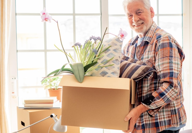 Homem sênior bonito sorridente segurando caixa de papelão posando em casa nova no dia da mudança