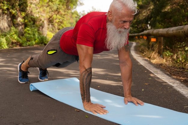 Homem sênior com barba branca fazendo exercícios na natureza conectando-se via laptop novo conceito de distanciamento normal e social