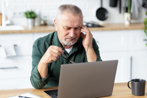 Homem sênior com forte dor de cabeça enquanto trabalhava em um laptop