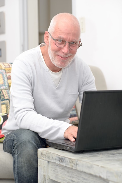 Homem sênior com laptop sentado no sofá