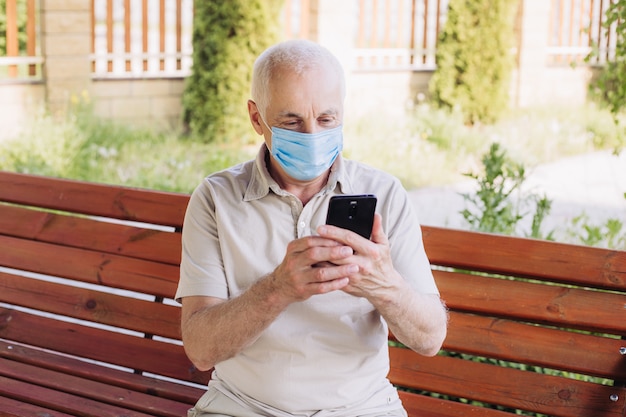 Homem sênior com máscara médica usando o telefone para procurar notícias. poluição do ar. conceito de quarentena de coronavírus.