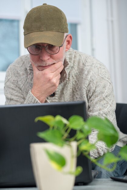 Homem sênior com tampa usando o laptop em casa