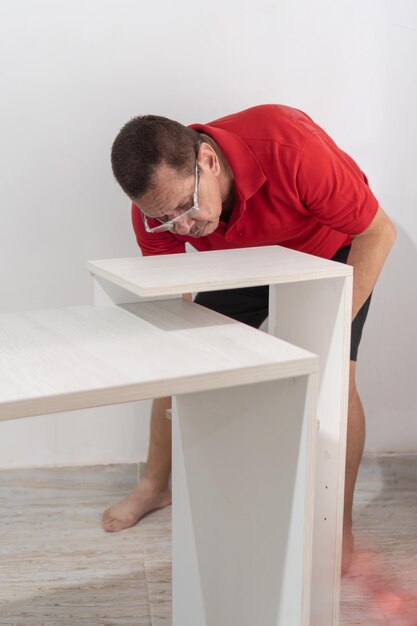 Homem sênior de camisa vermelha se concentrando no alinhamento de peças de mesa envolvendo-se em trabalho DIY preciso