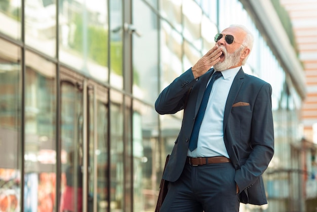 Homem sênior de negócios boceja ao ar livre Empresários sênior cansados caminhando ao ar livre