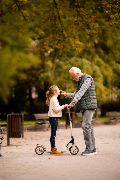 Homem sênior ensinando sua neta a andar de scooter no parque