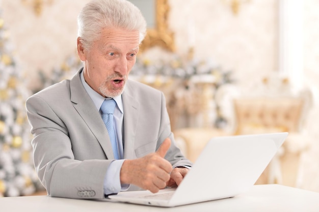 Homem sênior feliz trabalhando com laptop em casa