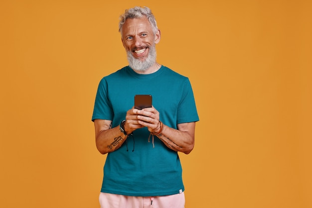 Homem sênior feliz usando telefone inteligente e sorrindo