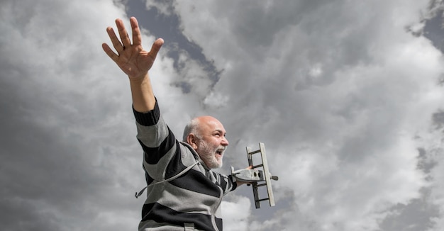 Homem sênior grisalho no fundo do céu homem sênior na aposentadoria homem aposentado sênior com avião de brinquedo