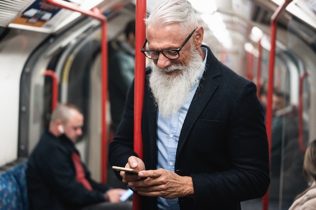 Homem sênior hippie feliz assistindo smartphone no metrô. Foco no rosto