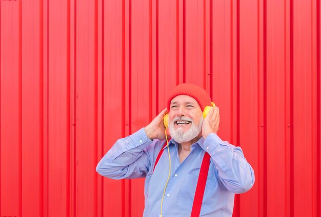 Homem sênior hipster feliz ouvindo música de lista de reprodução no fundo vermelho