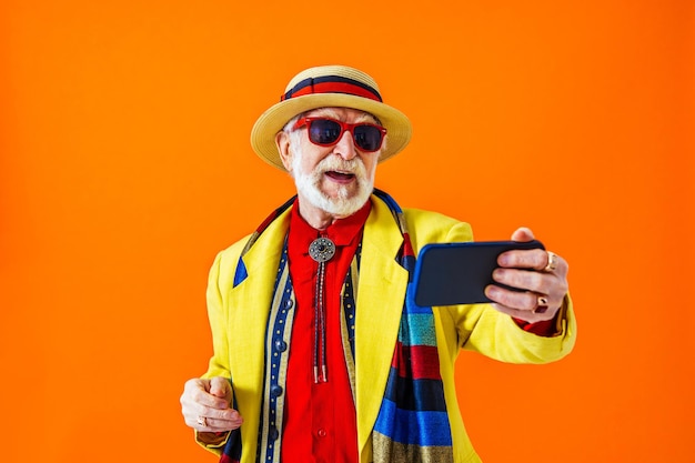 Homem sênior legal com retrato de estilo de roupas da moda em fundo colorido Velho aposentado engraçado com estilo excêntrico se divertindo