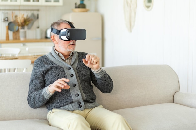 Homem sênior maduro animado usando fone de ouvido de óculos vr metaverse de realidade virtual em casa vovô