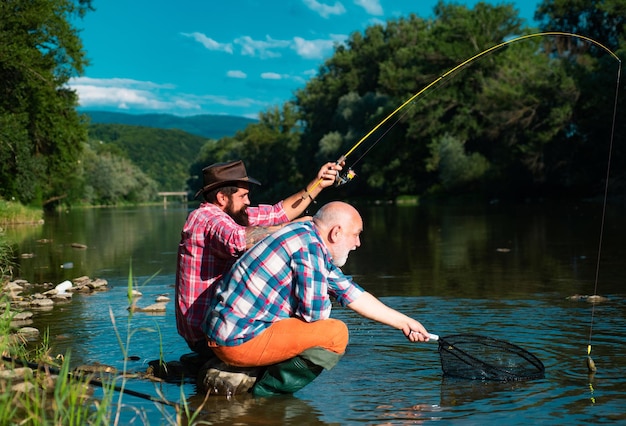 Homem sênior maduro com amigo pescando Férias de verão Pessoas alegres felizes Homens barbudos pegando peixe Pescador com vara de pescar Atividade e hobby