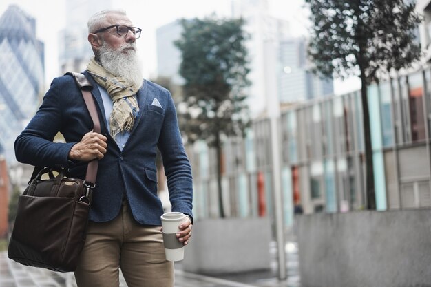 Homem sênior moderno de negócios em pé confiante enquanto bebe café num dia de inverno - foco no rosto