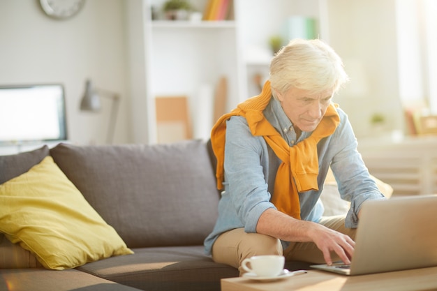 Homem sênior moderno usando o laptop em casa