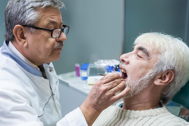 Homem sênior no dentista dentista ocupado com qualificação e experiência do paciente