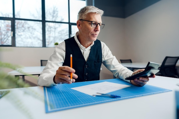 Homem sênior ocupado sentado na mesa do escritório com papéis e fazendo anotações