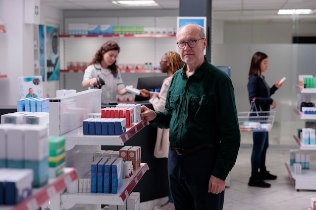 Homem sênior parado na farmácia na frente de prateleiras cheias de suplementos farmacêuticos. cliente alegre comprando vitamina, pílulas para curar doenças. serviço de apoio à saúde