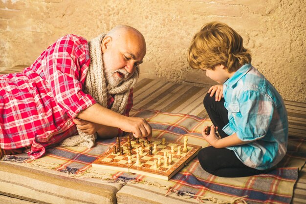 Homem sênior pensando em seu próximo movimento em um jogo de xadrez, garotinho jogando xadrez com seu avô ...