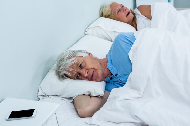 Homem sênior pensativo relaxante na cama com o telefone na mesa