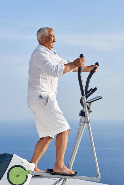 homem sênior saudável malhando na máquina de esteira de ginástica no terraço doméstico moderno com vista para o mar