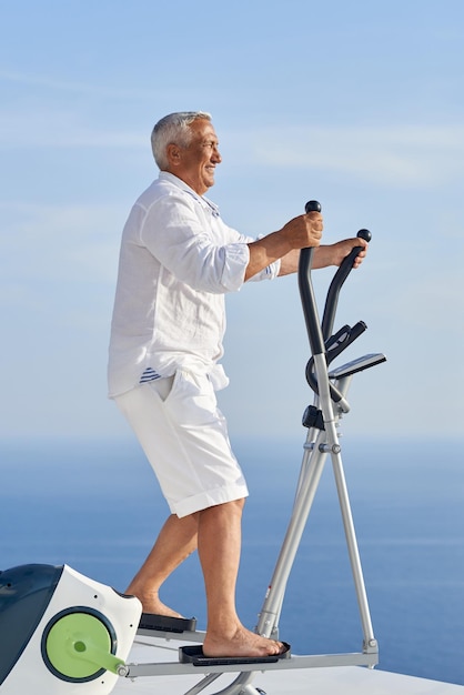homem sênior saudável malhando na máquina de esteira de ginástica no terraço doméstico moderno com vista para o mar