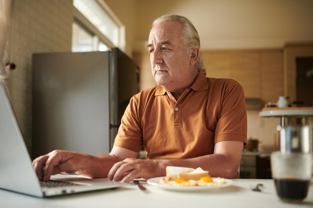 Homem sênior sério tomando café da manhã