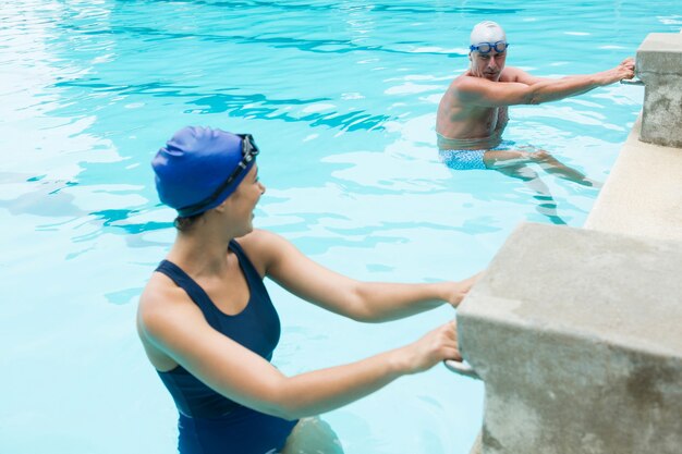 Homem sênior sorridente interagindo com mulher à beira da piscina