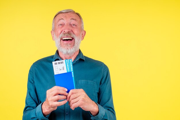 Homem sênior sorridente segurando passaporte na capa azul e fundo amarelo do estúdio de bilhetes.