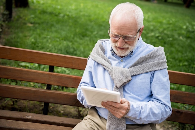 Homem sênior sorridente usando tablet digital enquanto está sentado no banco de madeira