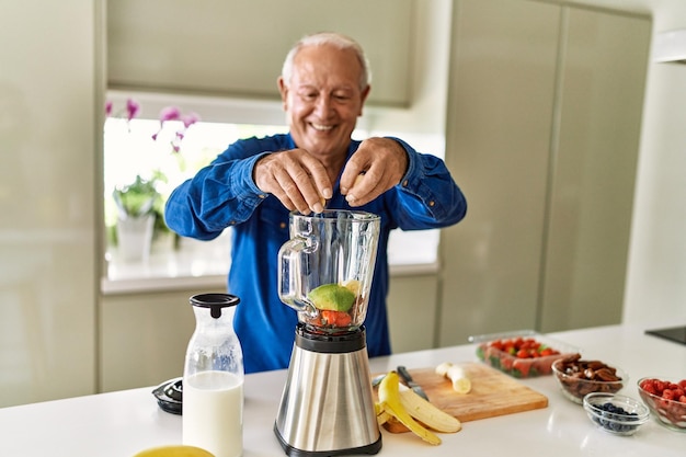 Homem sênior sorrindo confiante colocando banana no liquidificador na cozinha