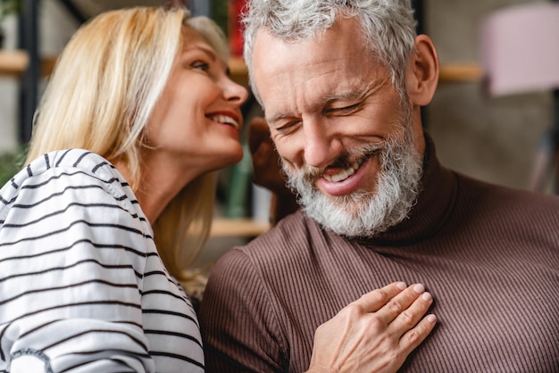 Homem sênior sorrindo enquanto sua linda esposa amorosa sussurrando em seu ouvido