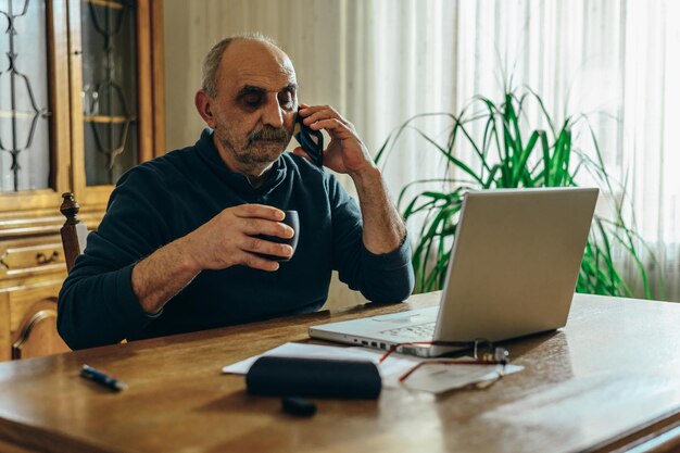 Homem sênior usando um smartphone e um laptop em casa