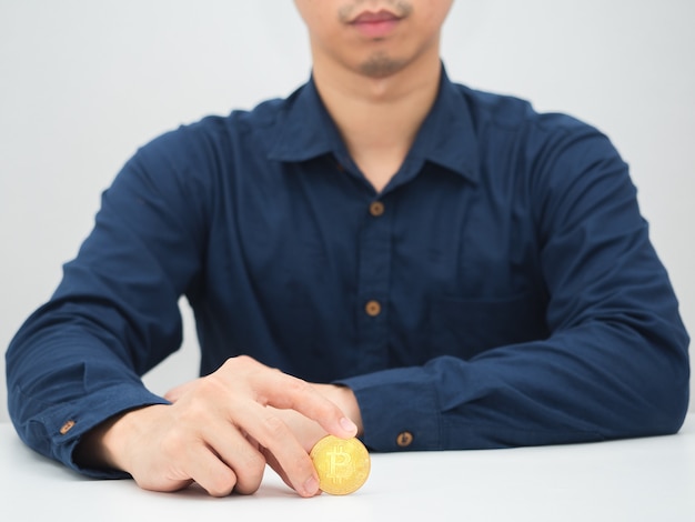 Homem sentado à mesa com bitcoin dourado na mão