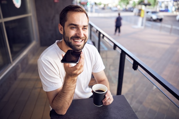 Foto homem sentado à mesa com smartphone e café