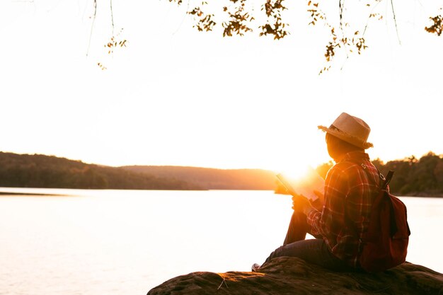 Foto homem sentado ao lado do lago contra o céu durante o pôr do sol