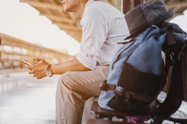 Homem sentado com celular e bolsa esperando trem. Conceito de trabalho e viagens.