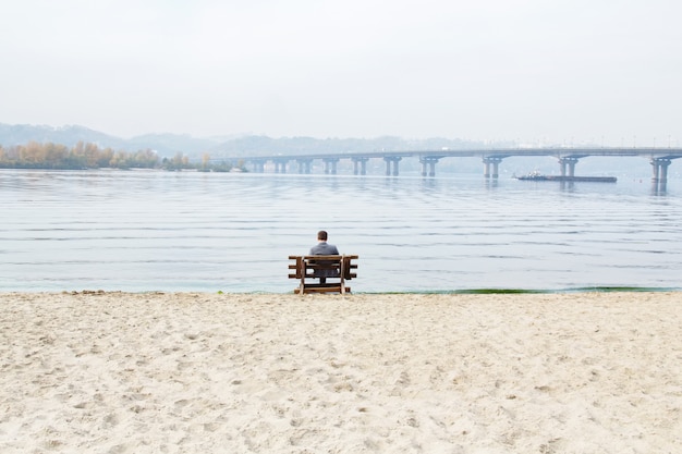 Homem sentado em um banco à beira do rio