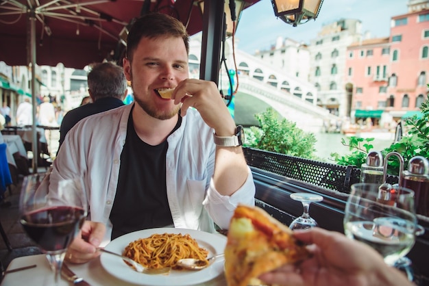 Homem sentado em um café, comendo macarrão, bebendo vinho, ponte, rialto, fundo, veneza, itália, restaurante ao ar livre