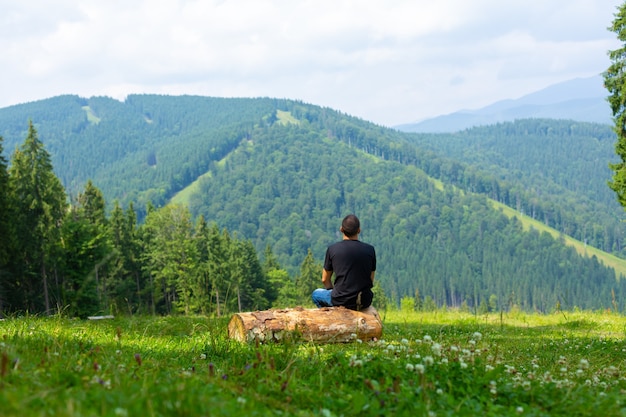 Homem sentado em um tronco apreciando a paisagem pacífica das montanhas verdes