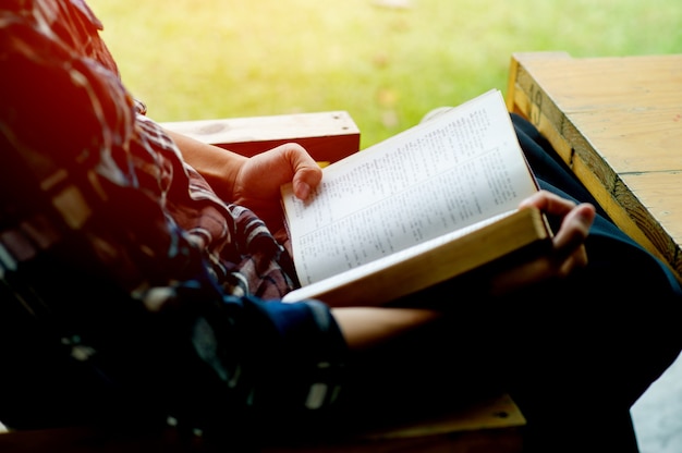 Homem sentado em uma cadeira vintage na frente de sua casa em um dia de descanso, leia um livro e relaxe. fundo desfocado. efeito de filme horizontal. o conceito de leitura de livros para aumentar o autoconhecimento.