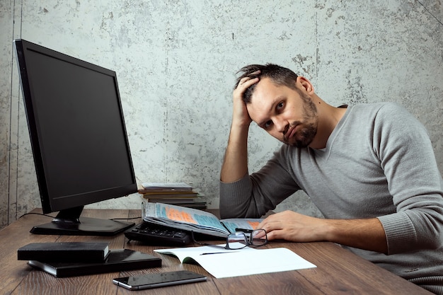 Homem sentado em uma mesa no escritório, e não está funcionando, parece cansado.