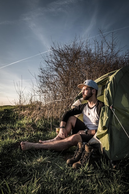 Foto homem sentado em uma tenda no campo durante o pôr do sol