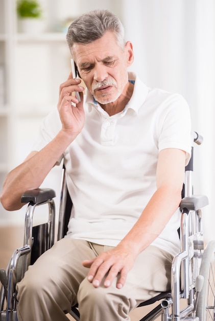 Homem sentado na cadeira de rodas em casa e falando no telefone.