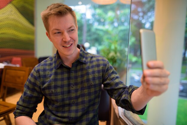 Homem sentado na cafeteria enquanto estiver usando o celular para tirar uma selfie